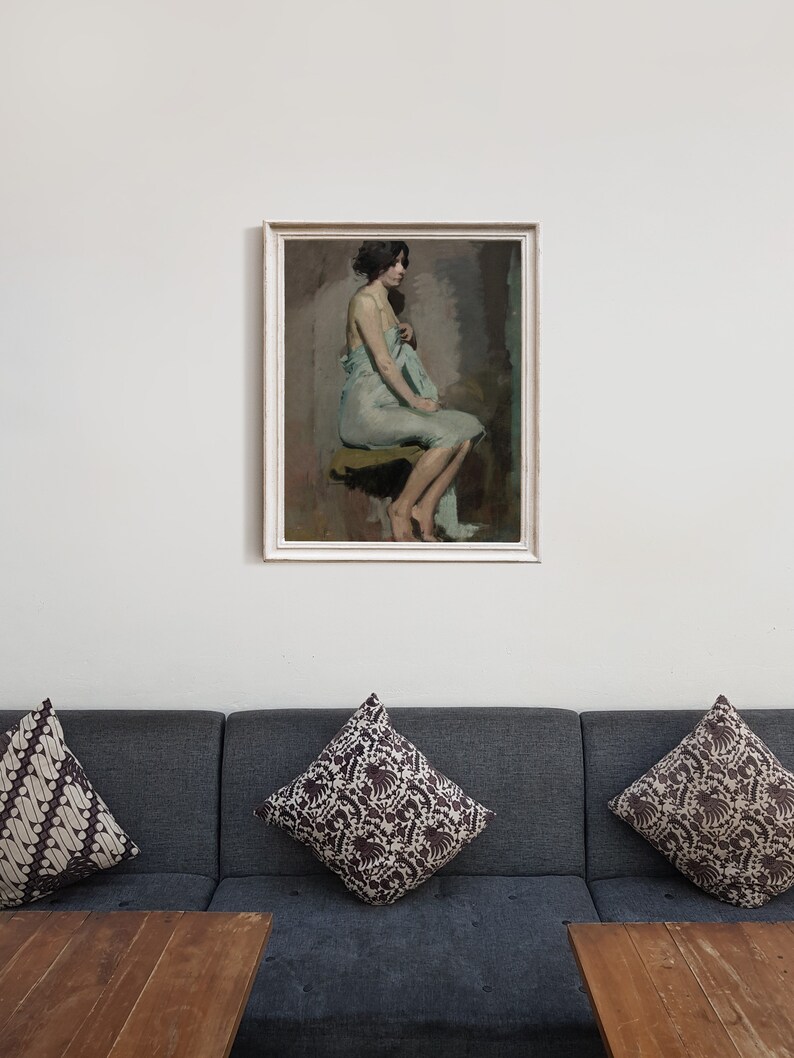 May include: A framed painting of a woman in a light blue dress sitting on a stool. The woman is looking to the side and has dark hair. The painting is set against a white wall.
