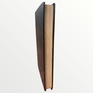 May include: A hardcover book with a black cover and tan-colored pages. The book is standing upright, showcasing the spine and the edge of the pages. The cover appears to be slightly worn.