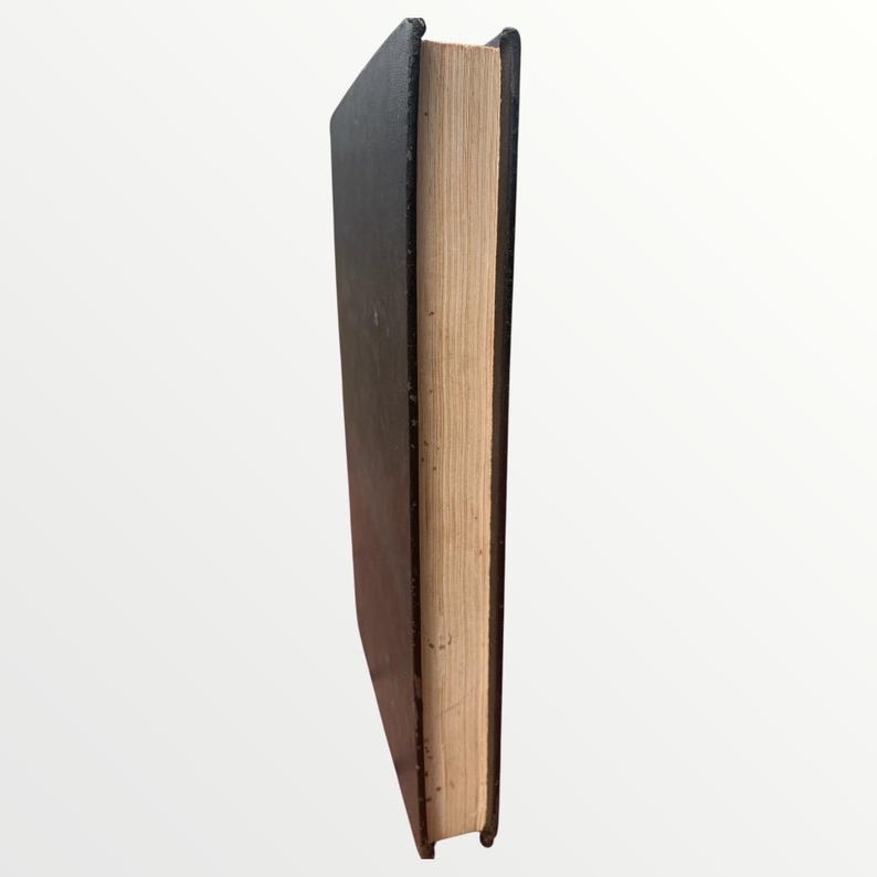 May include: A hardcover book with a black cover and tan-colored pages. The book is standing upright, showcasing the spine and the edge of the pages. The cover appears to be slightly worn.