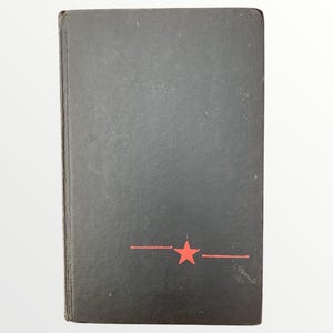 May include: A black book with a red star and two horizontal lines. The book has a worn appearance and a slightly textured surface. The cover is a solid black color.