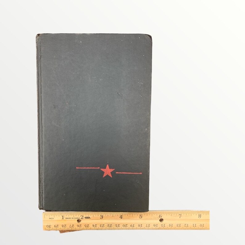 May include: A black book with a red star and line design. The book is next to a wooden ruler. The ruler is marked with inches and numbers from 1 to 30.