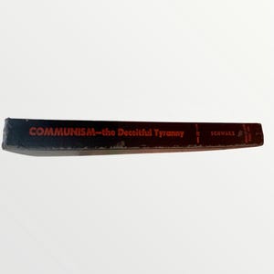 May include: A vintage book spine with the title "COMMUNISM-the Deceitful Tyranny" in red lettering. The book has a black cover and the author's name, "SCHWARZ", is also visible. The book is set against a white background.