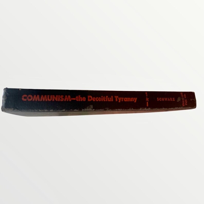 May include: A vintage book spine with the title "COMMUNISM-the Deceitful Tyranny" in red lettering. The book has a black cover and the author's name, "SCHWARZ", is also visible. The book is set against a white background.