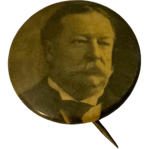 May include: Vintage pinback button featuring a portrait of a man with a mustache and dark suit. The button has a sepia tone and a pin on the back. The button is round and has a glossy finish.