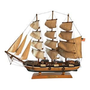May include: A detailed wooden model of a tall ship with multiple sails and rigging. The ship has a brown hull, black accents, and tan sails. An American flag is visible on the stern. The base reads "Pride of Baltimore II".