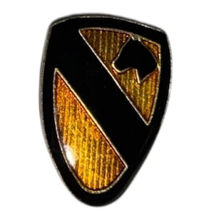 May include: A shield-shaped pin in black and gold, featuring a horse head silhouette. The pin has a black diagonal stripe and gold sections with a textured pattern. The edges are silver.