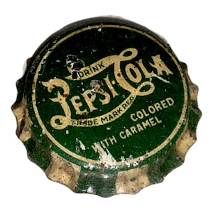 Könnte beinhalten: Vintage Pepsi Cola-Flaschenverschluss mit grünem und goldenem Design. Der Verschluss zeigt das Pepsi Cola-Logo und den Text "Drink Pepsi Cola, Trade Mark Reg, gefärbt mit Karamell."