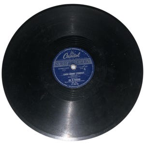 Puede incluir: Un disco de vinilo negro con una etiqueta azul que dice "Capitol Superflex" y "Little Johnny Strutout" de Joe Di Maggio. El disco tiene un diámetro de 30,5 cm.