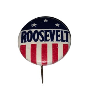 Könnte beinhalten: Ein Vintage-Wahlkampfknopf mit patriotischem Design. Der Knopf zeigt den Namen "ROOSEVELT" in fetten weißen Buchstaben auf weißem Hintergrund mit roten Streifen. Der obere Teil ist marineblau mit weißen Sternen.