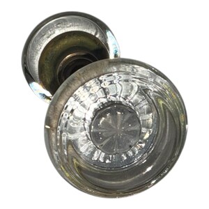 May include: A round, clear glass door knob featuring a faceted, star-like pattern at its center. The knob has a smooth, curved outer edge and is attached to a metallic base, showcasing a reflective, transparent design with intricate light-catching details.