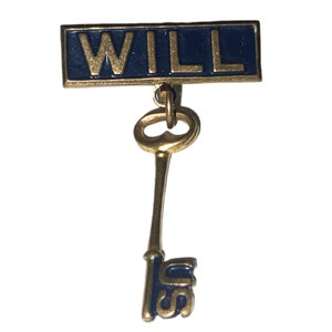 May include: A gold-colored key with a blue enamel tag that reads "WILL" hanging from it. The key has a blue enamel inscription on the bottom that reads "IS".