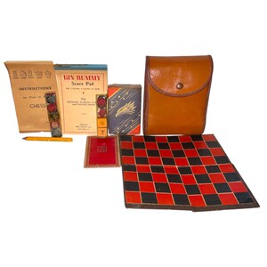 May include: A vintage game set featuring a red and black checkerboard, a brown leather case, and various game pieces. Includes a chess instruction booklet, a Gin Rummy score pad, and a pencil. The set is arranged on a white surface.