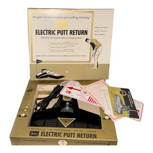 May include: A vintage Sears Electric Putt Return golf practice device in its original cardboard box. The set includes a black plastic putting return mechanism with a power cord, instructional pamphlets, and a putting guide. The box features gold and white graphics with text detailing the automatic ball return function for home practice.