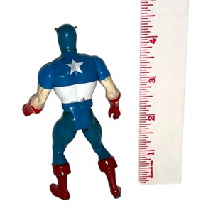 May include: A vintage Captain America action figure, viewed from the back, with a blue, white, and red color scheme. The figure has a white star on its back, red boots and gloves, and measures approximately 4 inches in height.