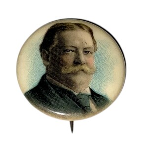 May include: A vintage round pin featuring a portrait of a man with a large mustache. The portrait is in color, with a light blue background and a pin backing.