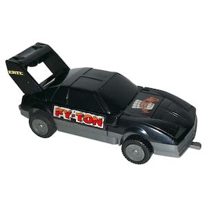 May include: Black and grey toy car with the text "FY-TON" in red and orange on the side. The car has a spoiler and the text "ERTE" on the spoiler. The front of the car has the text "SHOWDOWNS" in orange.