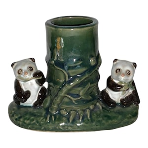 May include: A ceramic panda bear ornament featuring a dark green bamboo-shaped vase. Two panda bears with black and white fur sit either side of the vase. The vase and base are a dark green colour.