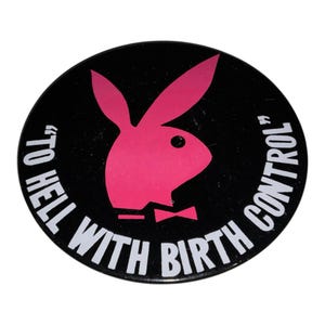 Peut inclure: Un bouton rond noir avec un logo de lapin rose et le texte blanc "TO HELL WITH BIRTH CONTROL". Le logo du lapin est une silhouette stylisée avec de longues oreilles et un nœud papillon.