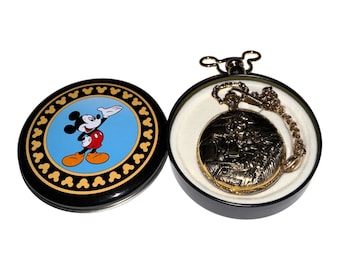 Könnte beinhalten: Eine goldfarbene Taschenuhr mit einem komplizierten Prägemuster und einer passenden Kette, die in einer schwarzen runden Dose liegt. Der Dosendeckel zeigt einen blauen Mittelkreis mit einer bunten Mickey-Mouse-Illustration und einen schwarzen Rand.