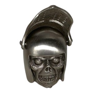 May include: A silver-toned ring shaped like a medieval helmet with a skull face. The helmet has a visor and is detailed with rivets and textures. The skull has visible teeth and eye sockets.