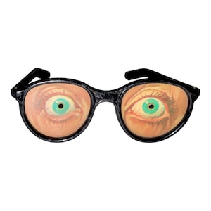 May include: Novelty glasses with black frames and lenses displaying a graphic of an eye with a green iris. The glasses have an oval shape and black arms. The eye graphic has a realistic appearance.