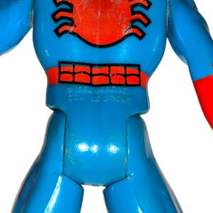 May include: Close-up of a vintage action figure, predominantly blue with red accents. The figure has a red spider emblem on the chest and a grid-like design. The text "&copy; 1984 MARVEL COMICS GROUP" is visible.
