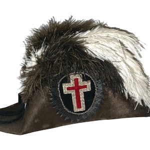 May include: A brown felt hat with a white and brown feather plume. The hat has a silver and red cross emblem on the front.