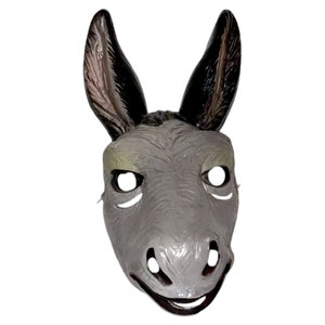 May include: A gray donkey mask with large, upright ears and a smiling expression. The mask has eye and nose openings, and is likely made of plastic or a similar material. The ears are black on the inside and the mask is set against a white background.