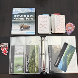 May include: A guidebook titled Your Guide to the National Parks, a spiral-bound passport book with circular date stamps, a Petrified Forest sticker, a three-ring binder with clear sleeves, and brochures for Gulf Islands, George Washington Memorial Parkway, Cumberland Gap, Shenandoah, and an Acadia National Park sticker.