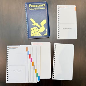 May include: A blue Passport To Your National Parks booklet with a yellow eagle and star graphic, accompanied by several white spiral-bound insert pages featuring colored tabs and designated rectangular spaces for official regional stamps.