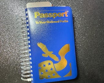 May include: A blue passport-style notebook with a gold eagle and stars design. The cover reads "Passport to Your National Parks".