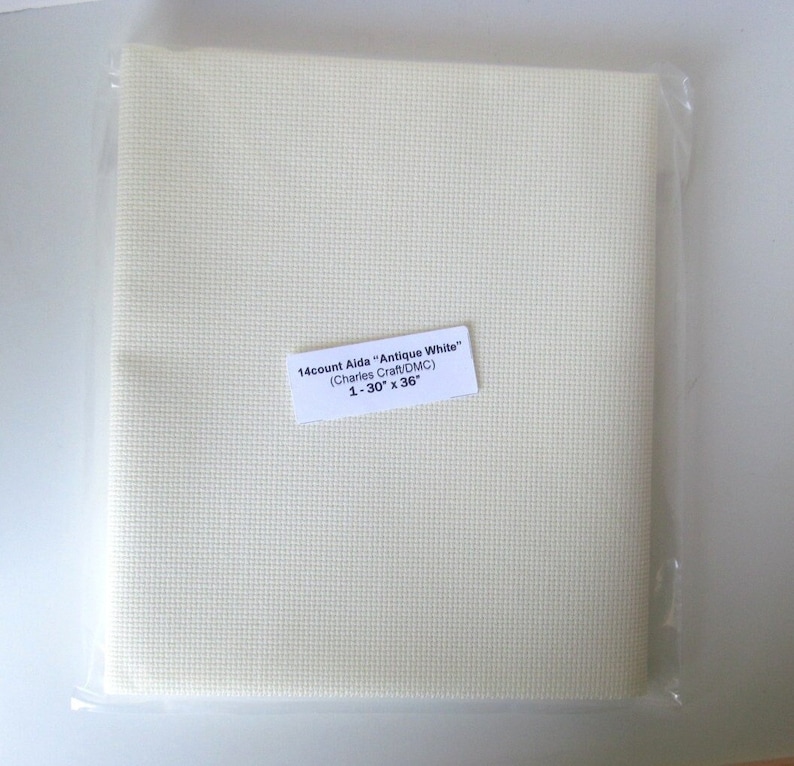 May include: Aida cloth in a clear plastic package. The fabric is antique white and has a grid-like texture. A label indicates it is 14-count Aida, 30 x 36 inches, from Charles Craft/DMC.