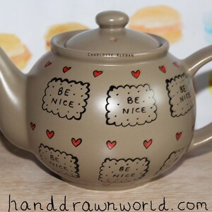 May include: A brown teapot with a lid, decorated with red hearts and black outlines of biscuits that say "Be Nice".
