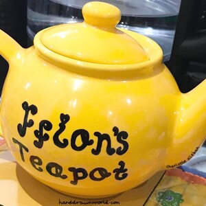 Pode incluir: Uma chaleira amarela com letras pretas que dizem "Flon's Teapot".