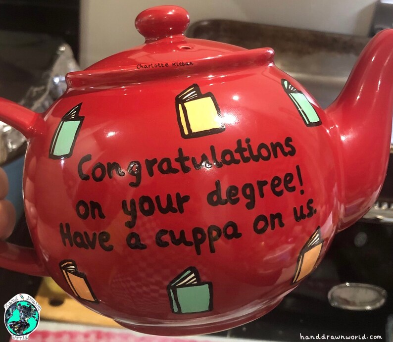 May include: Red teapot with a black inscription that reads "Congratulations on your degree! Have a cuppa on us." The teapot is decorated with colourful book illustrations.