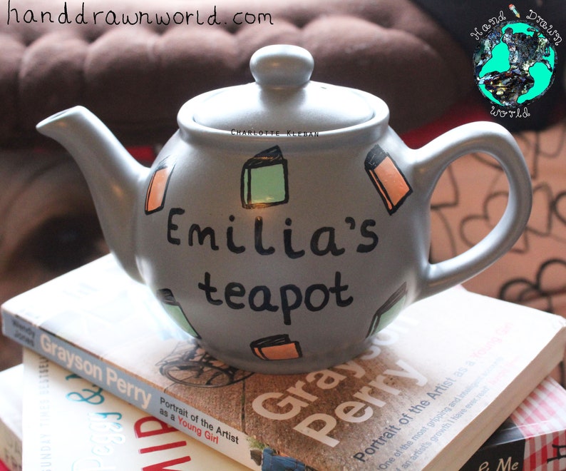 May include: A grey teapot with the words "Emilia's teapot" painted on it. The teapot is decorated with colourful book illustrations.