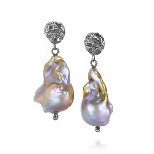 May include: A pair of elegant dangle earrings. Each earring features a large, iridescent baroque pearl suspended from a textured silver-tone stud. The pearls display a mix of colors, including pink, gold, and lavender, with a small silver accent at the bottom.