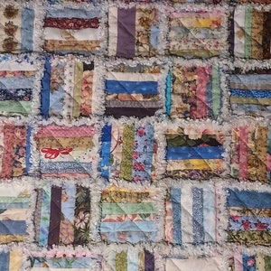 May include: A patchwork quilt with a variety of colorful fabrics and patterns. The quilt is made up of squares, each with a different design. The quilt is made with a rag quilt technique, which gives it a unique and textured look.