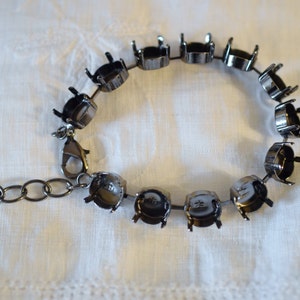 May include: A gunmetal-colored bracelet with multiple round settings designed to hold gemstones. The bracelet has a lobster clasp closure and an extender chain for adjustable sizing. The settings are empty, ready for customization.