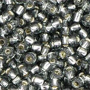 May include: A close-up image of a large quantity of small, round, silver-colored beads. The beads have a slightly iridescent finish and are arranged in a random pattern.