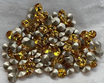 May include: A collection of sparkling, faceted rhinestones in shades of gold and silver. The gemstones are round and teardrop-shaped, with a metallic luster. These decorative embellishments are ideal for crafting and adding sparkle to various projects.