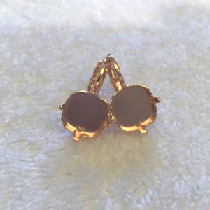 May include: A pair of gold-tone earring settings with a square shape. The settings are open on the back and ready to be filled with stones.