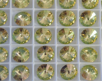 May include: A close-up view of a tray of round, faceted, green glass rhinestones. The rhinestones are arranged in a grid pattern and have a slight iridescent sheen.