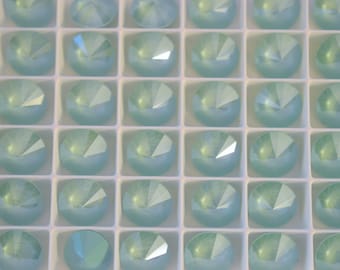 May include: Close-up of a tray filled with numerous light blue, faceted, round gemstones. Each gem is set in a square compartment, creating a grid-like pattern. The gems have a reflective, iridescent quality.