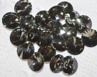 May include: A group of 18 round, faceted, dark green glass rhinestones. The rhinestones have a shiny, iridescent finish.