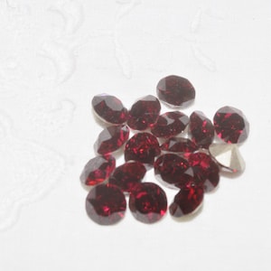 May include: A group of 16 small, round, red rhinestones. The rhinestones are faceted and have a shiny finish.