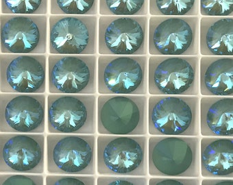 May include: A close-up view of a tray of light blue round rhinestones. The rhinestones are arranged in a grid pattern and are all the same size. The tray is white and has a grid pattern.