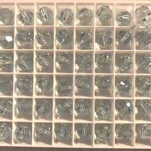 May include: A clear plastic container filled with 48 round, faceted, crystal beads. The beads are arranged in a grid pattern.