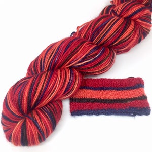 May include: A skein of colorful yarn with a knitted swatch. The yarn is primarily red with orange, blue, and black stripes. The knitted swatch displays the same color pattern. Ideal for knitting and crochet projects.