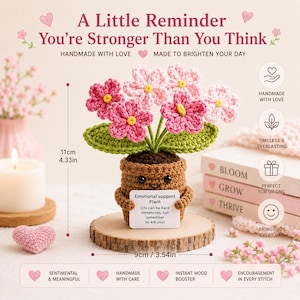 May include: A crocheted potted plant with pink and light pink flowers and green leaves in a brown pot. The pot features a small white sign that reads: Emotional support Plant. Life can be hard sometimes, but remember so are you! It is 11cm (4.33in) tall and 9cm (3.54in) wide.